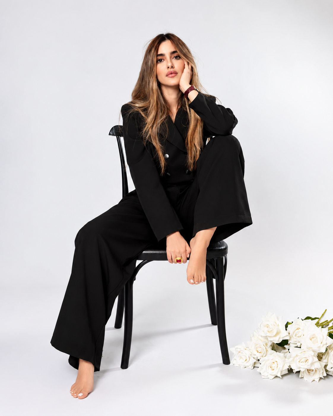 Aya Abaakil seated in black tailoring, white roses on a pale studio floor